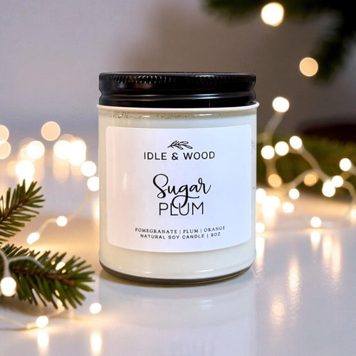 Sugar Plum candle labeled with decorative lights and greenery in the background