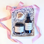 Gift set with a candle, spray, and bath bomb in a box with pink ribbon on a white background