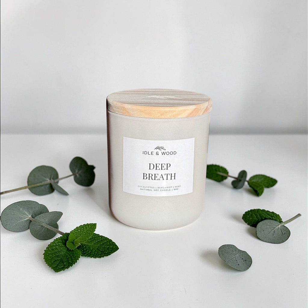 Candle labeled 'Deep Breath' with eucalyptus leaves on a white background