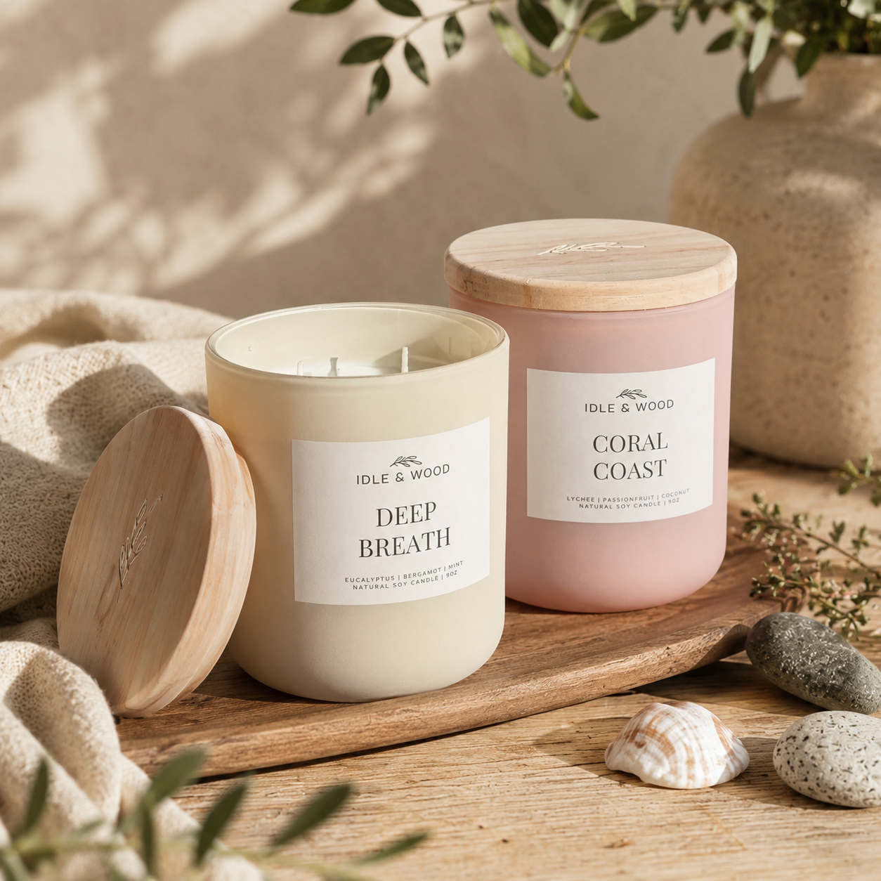 Idle & Wood Deep Breath and Coral Coast soy candles styled on a natural wood surface with soft greenery, seashells, stones, and warm neutral home decor.